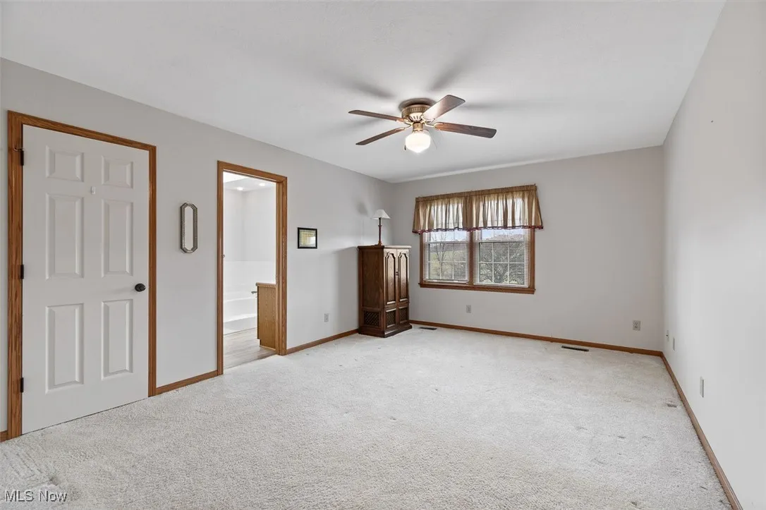 Unfurnished bedroom featuring carpet flooring, a ceiling fan, and ensuite bath