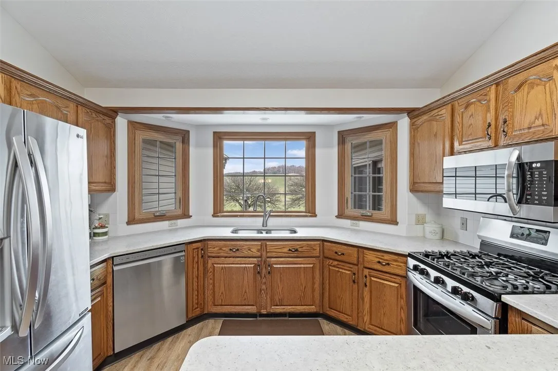 Kitchen with appliances with stainless steel finishes, brown cabinetry, light stone countertops, and light wood-style flooring