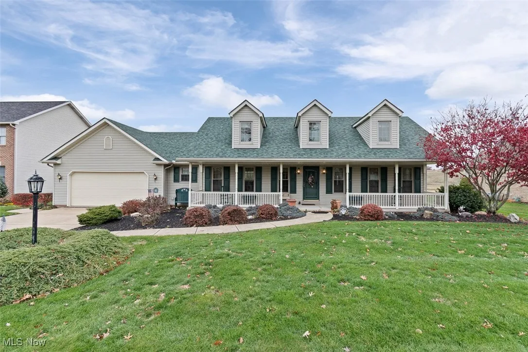 Cape cod home featuring covered porch, a shingled roof, a front yard, a garage, and concrete driveway