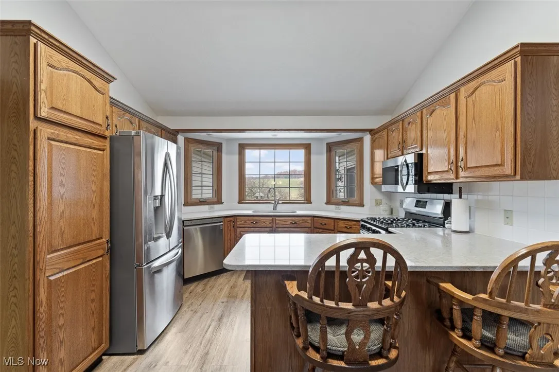 Kitchen with stainless steel appliances, tasteful backsplash, vaulted ceiling, brown cabinets, and light wood-type flooring