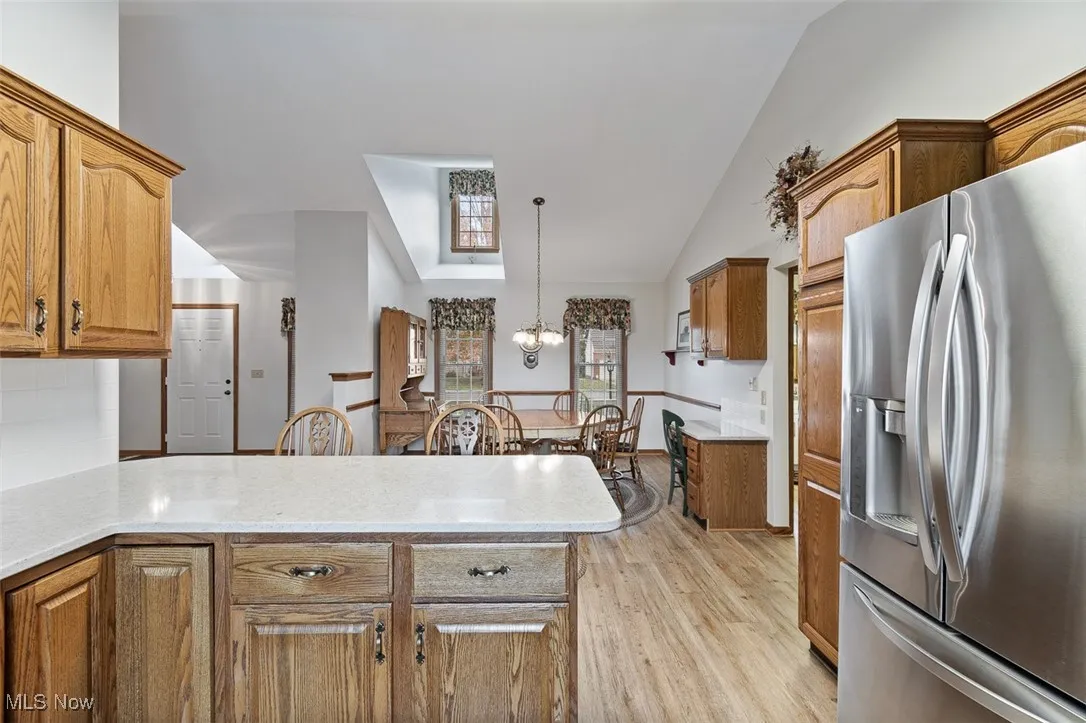 Kitchen with stainless steel fridge, pendant lighting, a chandelier, brown cabinets, and light stone counters