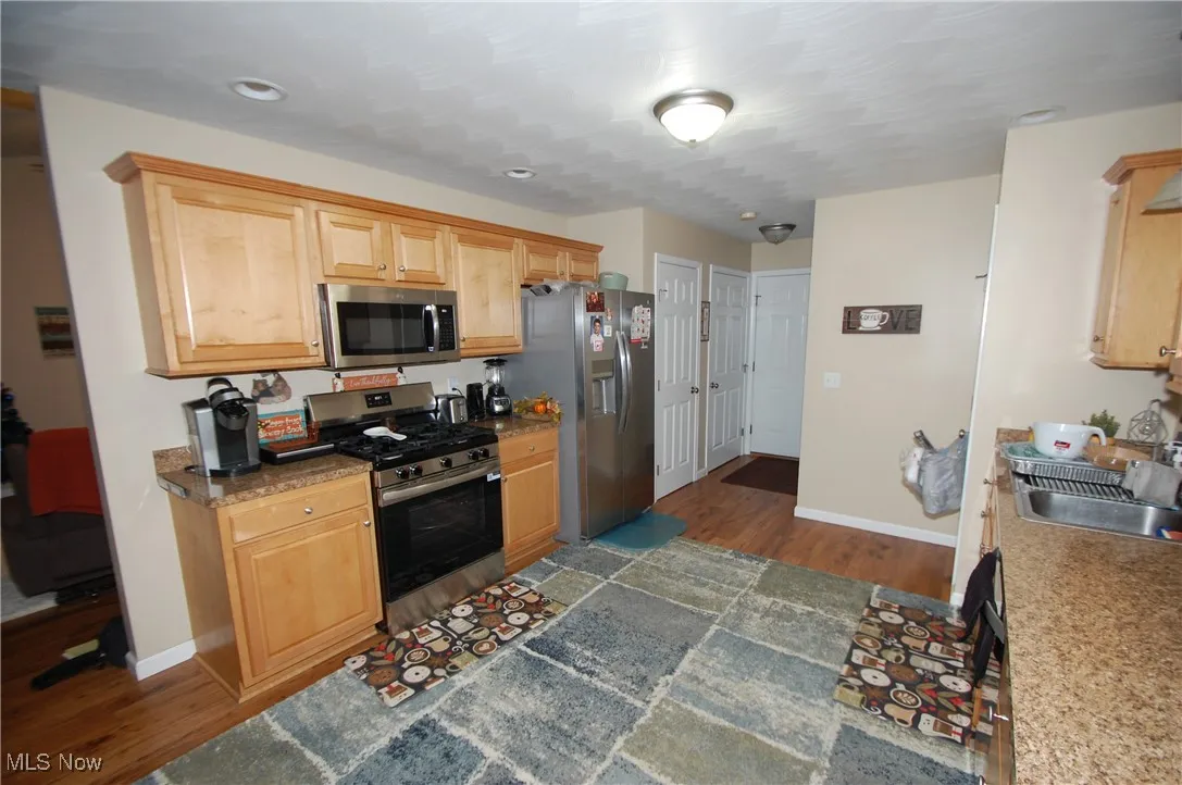Kitchen featuring stainless steel appliances, dark wood-style flooring, dark countertops, and light brown cabinets