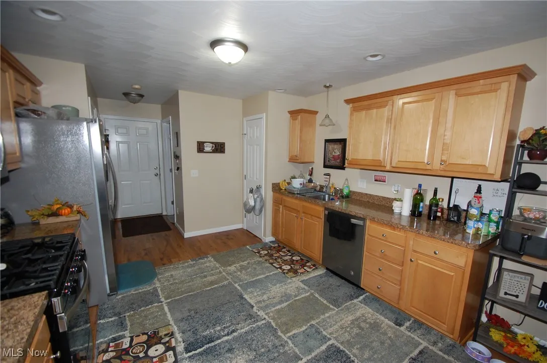 Kitchen with stainless steel appliances, stone tile flooring, dark stone counters, and hanging light fixtures