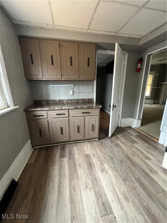 Kitchen featuring a drop ceiling, light wood finished floors, wood walls, and dark countertops