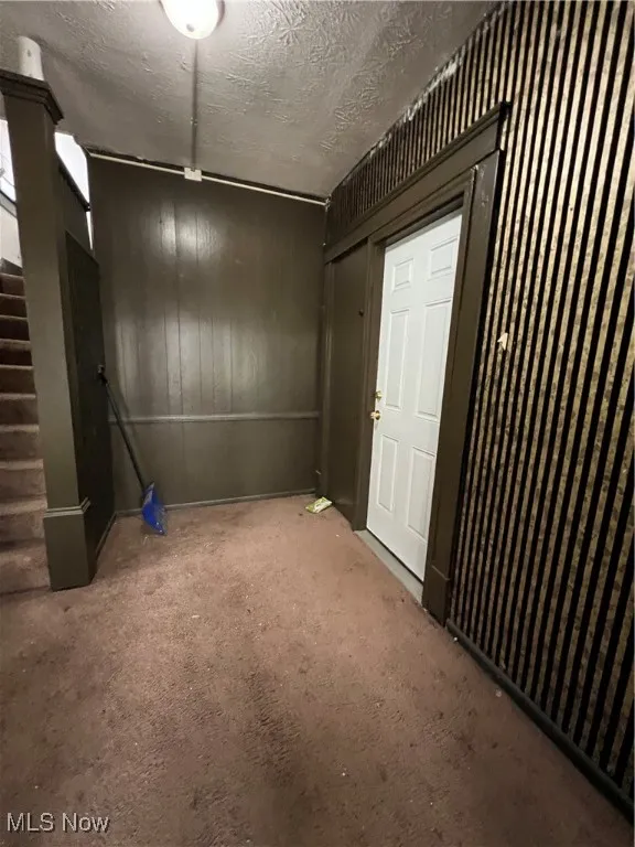 Carpeted spare room with a textured ceiling and stairs