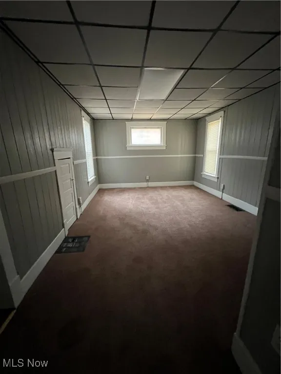 Basement with wooden walls, a drop ceiling, and carpet flooring