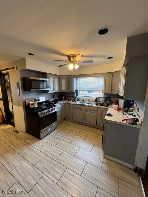 Kitchen with gray cabinets, stove, wainscoting, white microwave, and light countertops