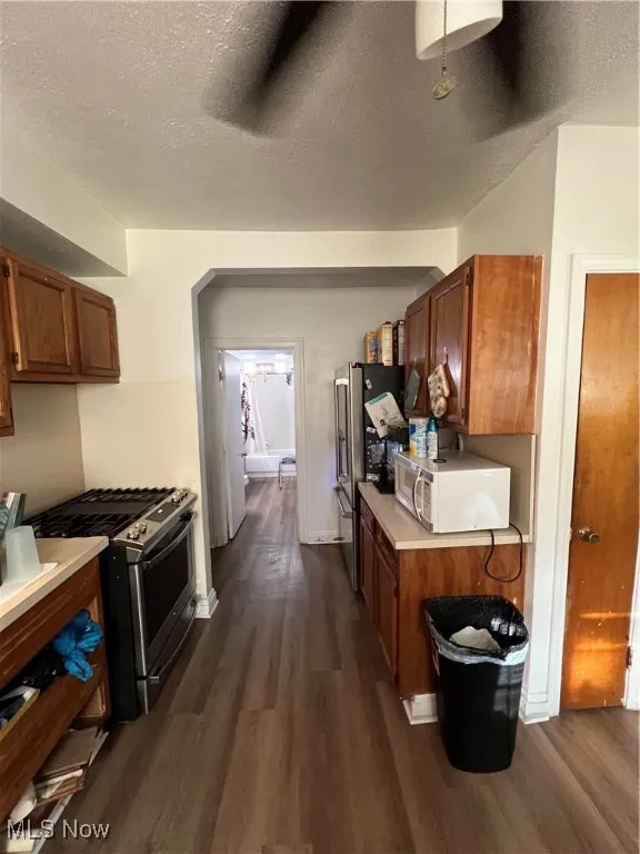 Kitchen with range, a textured ceiling, brown cabinets, light countertops, and dark wood-type flooring