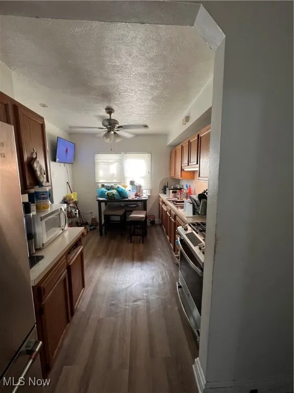 Kitchen featuring light countertops, fridge, dark wood finished floors, brown cabinetry, and ceiling fan
