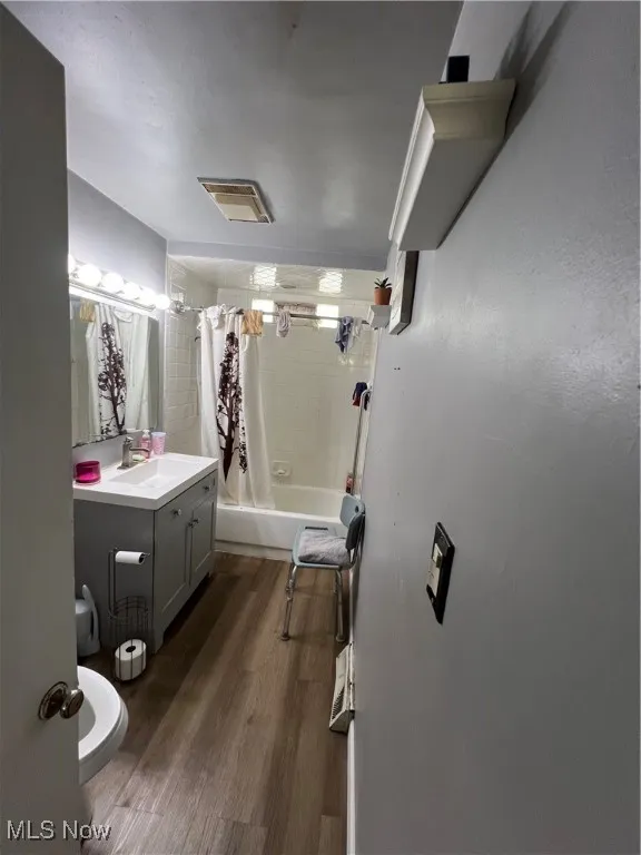 Full bathroom featuring shower / bathtub combination with curtain, vanity, and dark wood-style floors