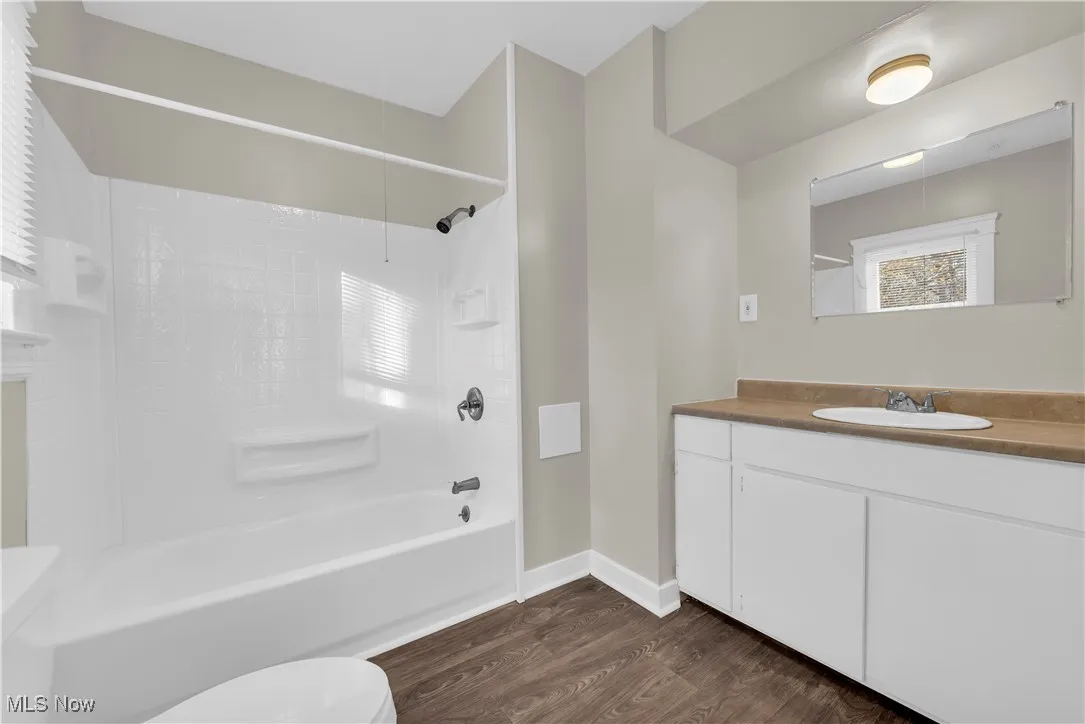 Full bath with vanity, shower / bathtub combination, healthy amount of natural light, and dark wood finished floors