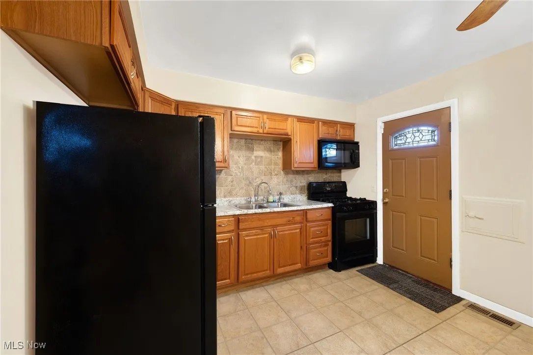 Kitchen featuring black appliances, brown cabinetry, tasteful backsplash, ceiling fan, and light tile patterned floors