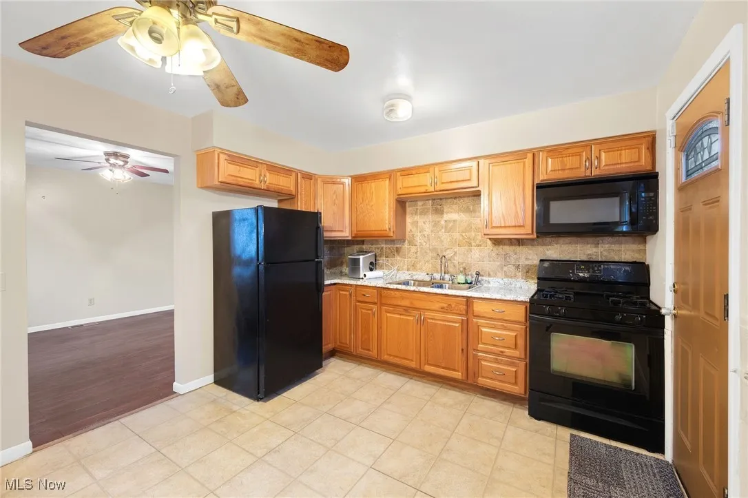 Kitchen featuring black appliances, backsplash, brown cabinets, ceiling fan, and light tile patterned floors