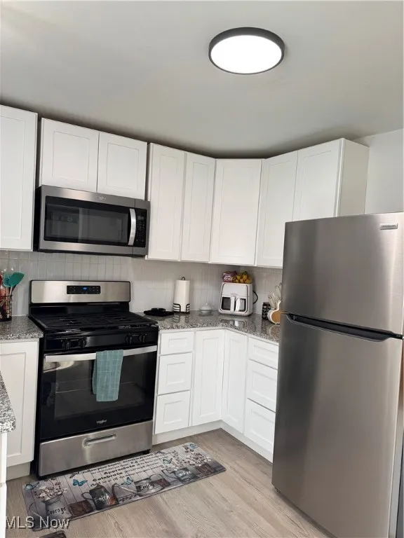 Kitchen featuring stainless steel appliances, light stone countertops, white cabinetry, light wood finished floors, and tasteful backsplash