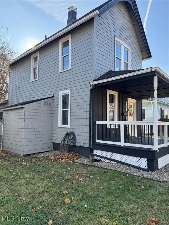 Rear view of house featuring covered porch, a yard, a chimney, and board and batten siding