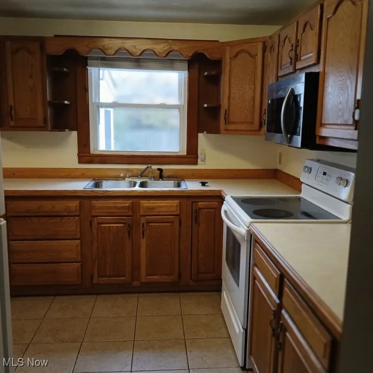 Kitchen featuring open shelves, white range with electric stovetop, light countertops, stainless steel microwave, and brown cabinets