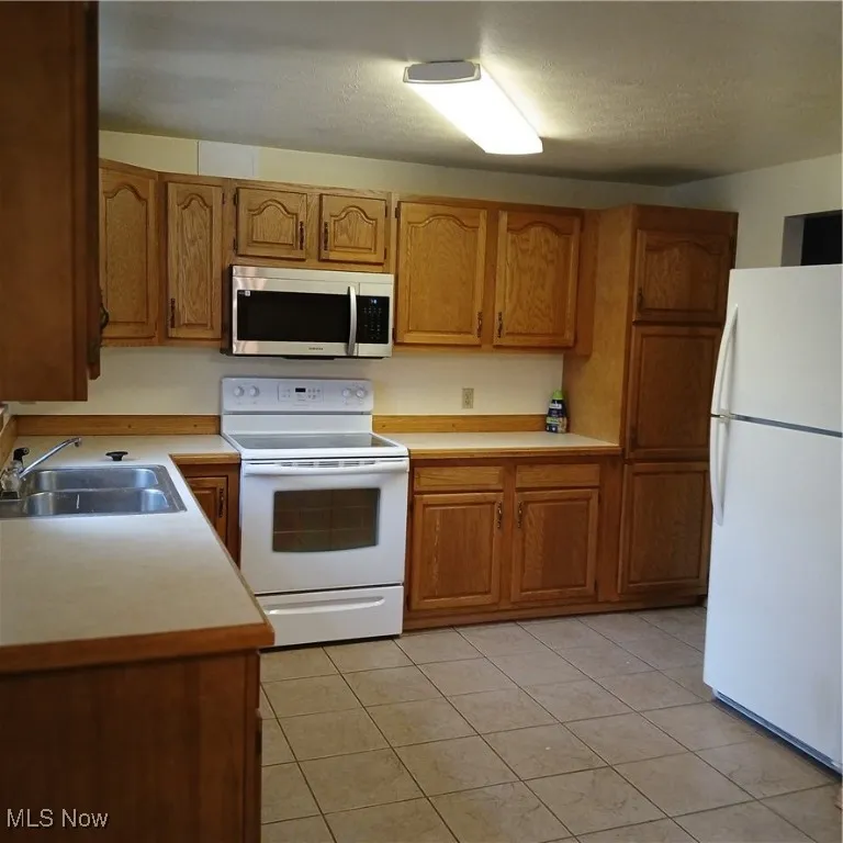 Kitchen featuring stainless steel range oven, light countertops, fridge, and brown cabinets