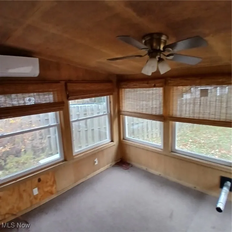 Unfurnished sunroom featuring healthy amount of natural light, a wall mounted AC, vaulted ceiling, and carpet flooring