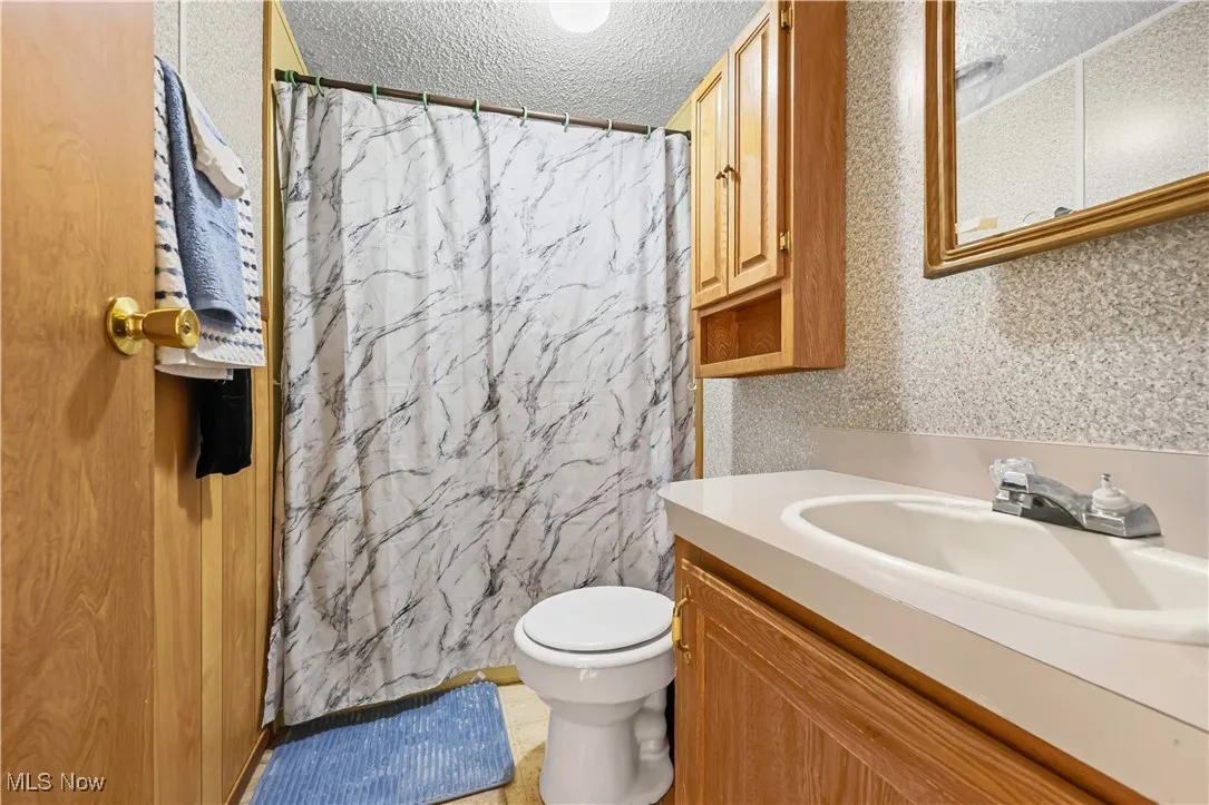 Bathroom with vanity, a textured ceiling, curtained shower, and wallpapered walls