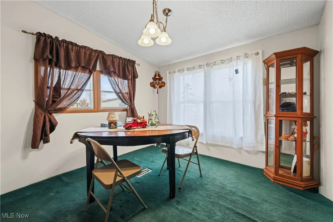 Dining area with a textured ceiling, vaulted ceiling, a chandelier, and dark colored carpet