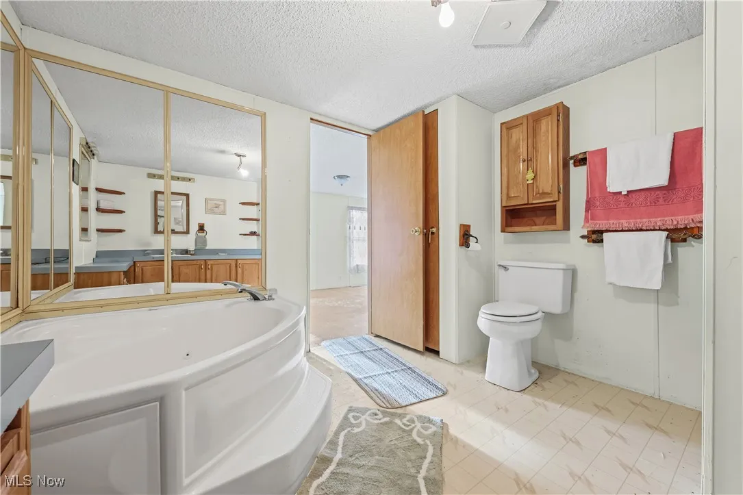 Full bathroom with a textured ceiling, a garden tub, vanity, and light flooring