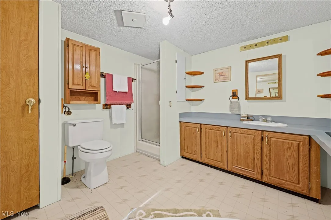 Bathroom with vanity, a stall shower, a textured ceiling, and light floors