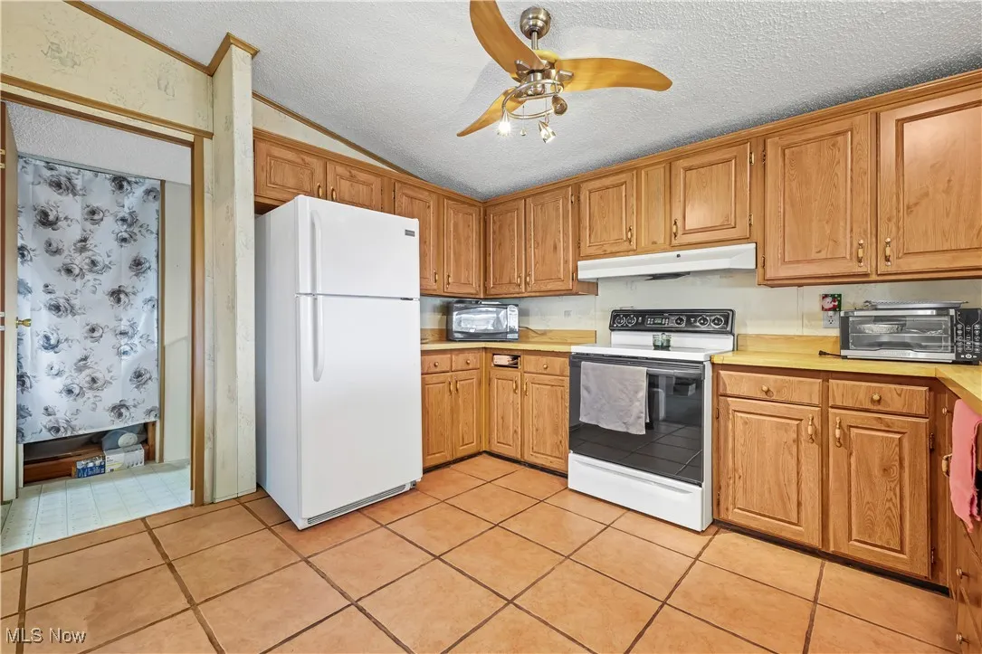 Kitchen with light countertops, white appliances, a textured ceiling, ceiling fan, and lofted ceiling
