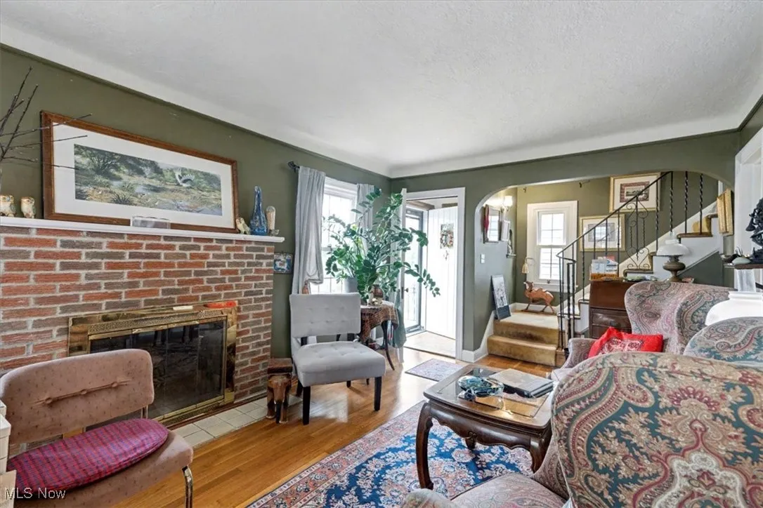 Living room with stairway, arched walkways, wood finished floors, a brick fireplace, and a textured ceiling