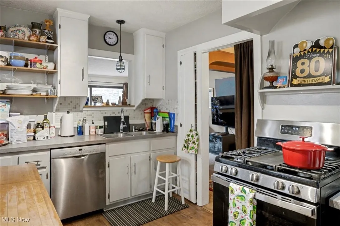 Kitchen featuring stainless steel appliances, white cabinetry, butcher block counters, decorative light fixtures, and open shelves