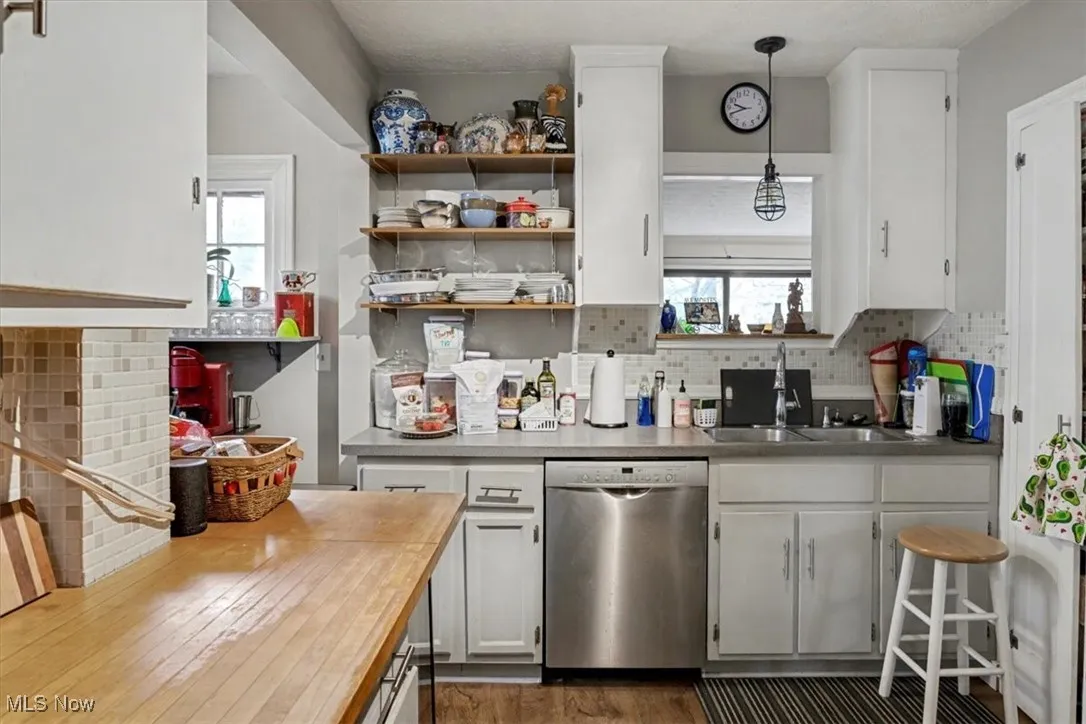 Kitchen featuring butcher block counters, dishwasher, white cabinets, decorative backsplash, and pendant lighting