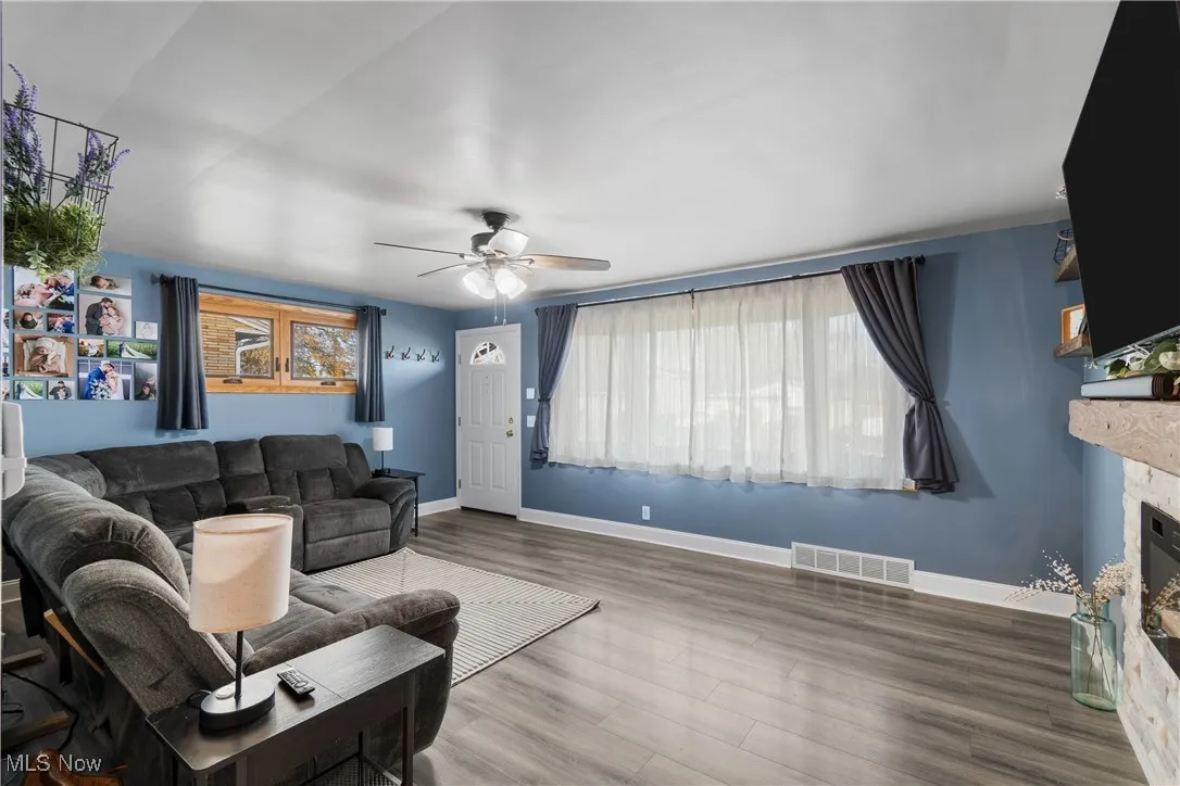 Living room with a stone fireplace, wood finished floors, and a ceiling fan