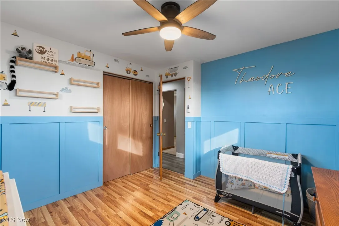 Bedroom with wainscoting, a decorative wall, light wood-style flooring, a closet, and ceiling fan
