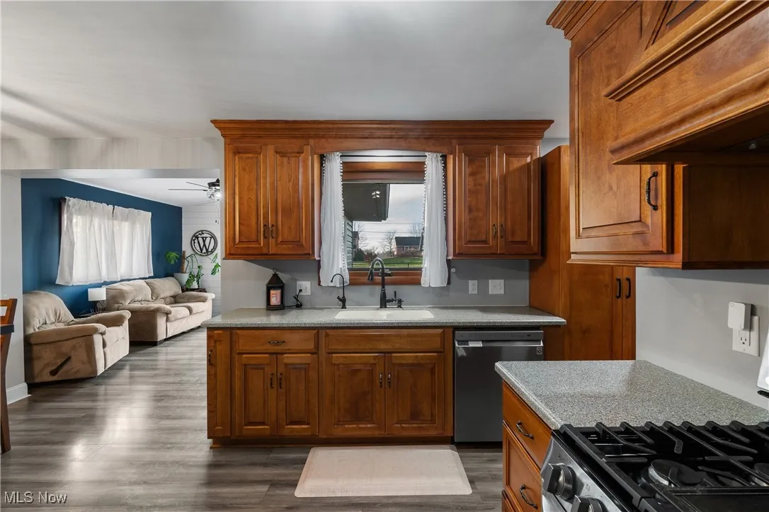 Kitchen featuring premium range hood, gas stove, stainless steel dishwasher, dark wood finished floors, and brown cabinetry