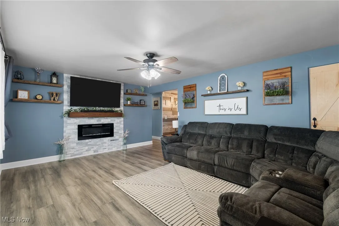 Living area with a ceiling fan, wood finished floors, and a fireplace