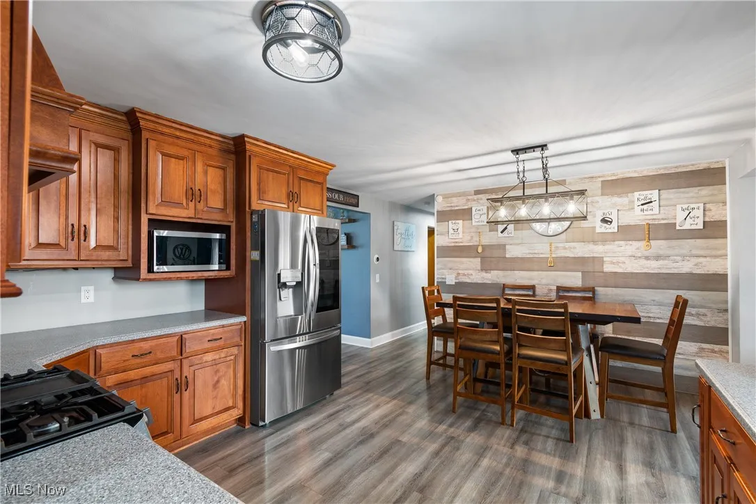 Kitchen featuring brown cabinetry, appliances with stainless steel finishes, an accent wall, wood walls, and light stone counters