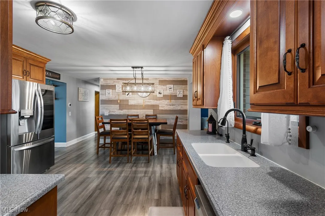 Kitchen with an accent wall, brown cabinetry, stainless steel appliances, light stone countertops, and wood walls