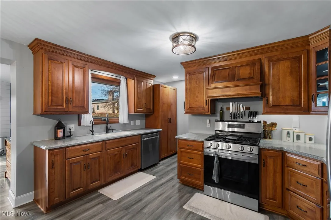 Kitchen with stainless steel appliances, brown cabinetry, custom exhaust hood, and recessed lighting