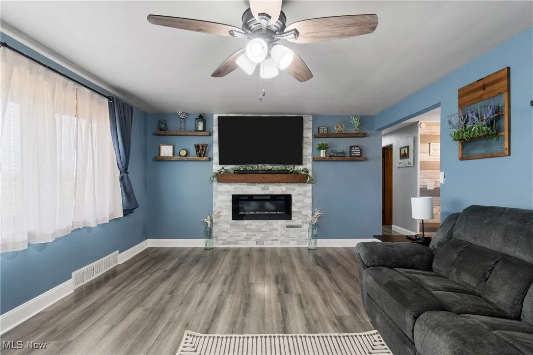 Living room with ceiling fan, a fireplace, and wood finished floors