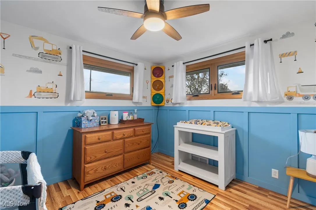 Bedroom with a ceiling fan, light wood-style flooring, and a decorative wall