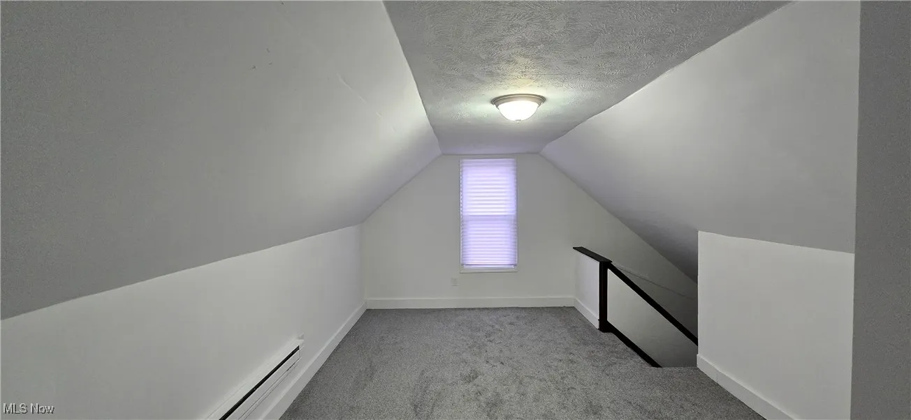 3rd level. Additional living space with a baseboard radiator, a textured ceiling, light colored carpet, and lofted ceiling