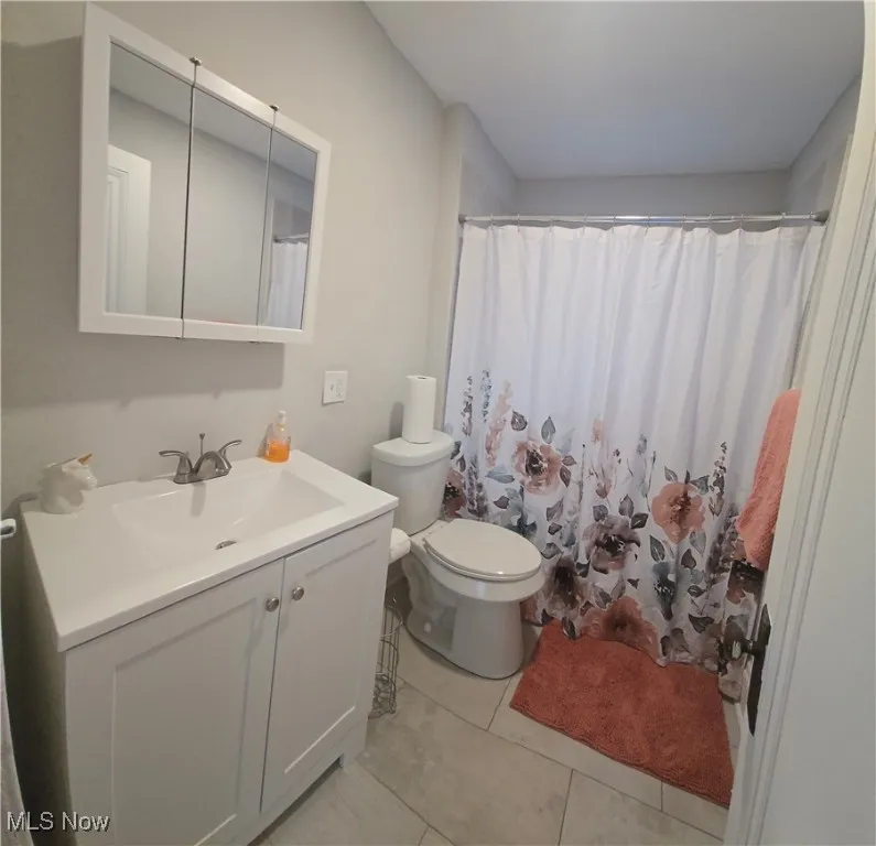 Full bath 1st level - with a shower with shower curtain, vanity, and light tile patterned floors