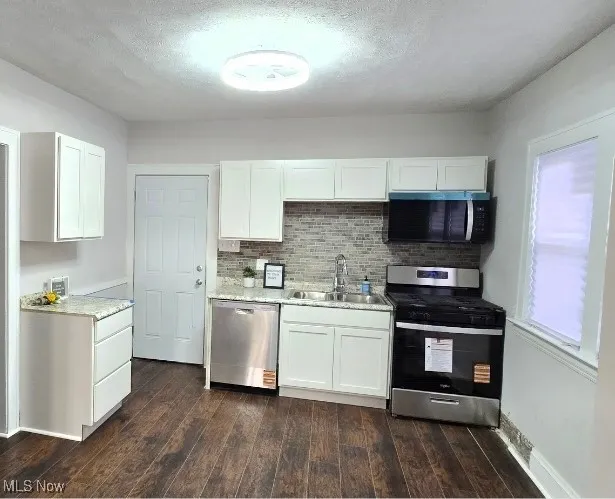 Kitchen 1st unit -featuring appliances with stainless steel finishes, white cabinetry, a textured ceiling, tasteful backsplash, and dark wood-type flooring