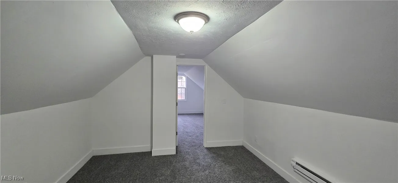 Bedroom 2. Additional living space featuring a textured ceiling, baseboard heating, dark colored carpet, and vaulted ceiling