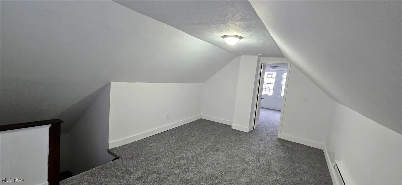 3rd level. Additional living space with dark carpet, lofted ceiling, baseboard heating, and a textured ceiling