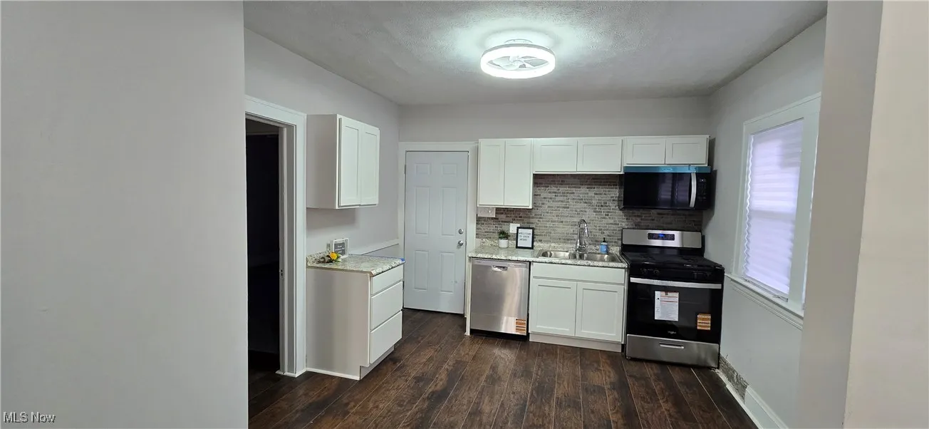 Kitchen 1st unit - featuring appliances with stainless steel finishes, white cabinets, backsplash, dark wood-type flooring, and a textured ceiling