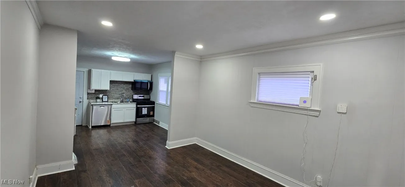 Kitchen open into living room on 1st level with white cabinets, appliances with stainless steel finishes, dark wood-type flooring, decorative backsplash, and recessed lighting