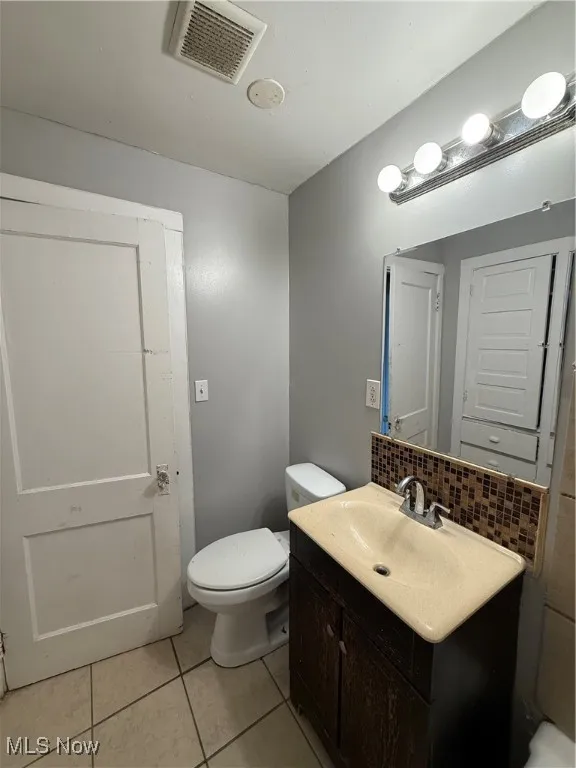 Half bathroom featuring decorative backsplash, vanity, and light tile patterned floors