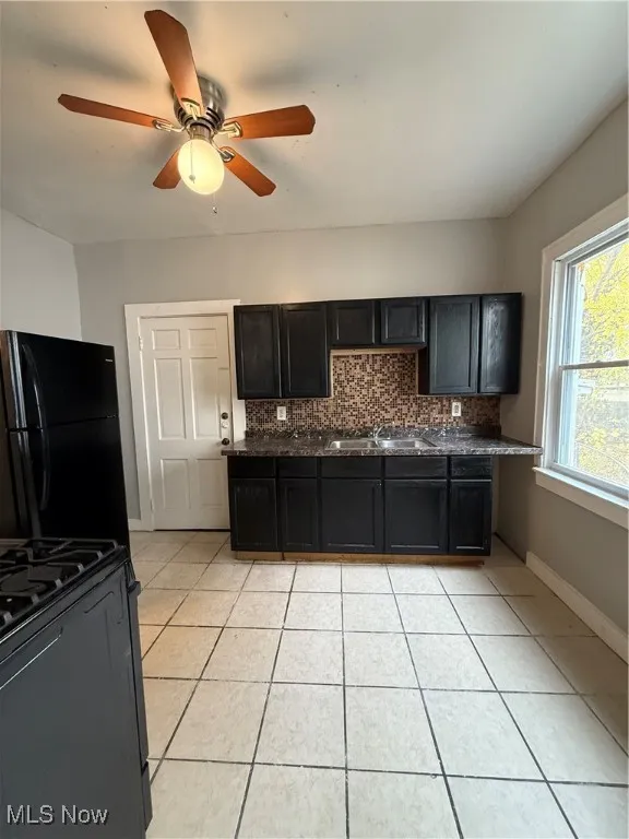 Kitchen featuring dark cabinetry, stove, fridge, tasteful backsplash, and light tile patterned floors
