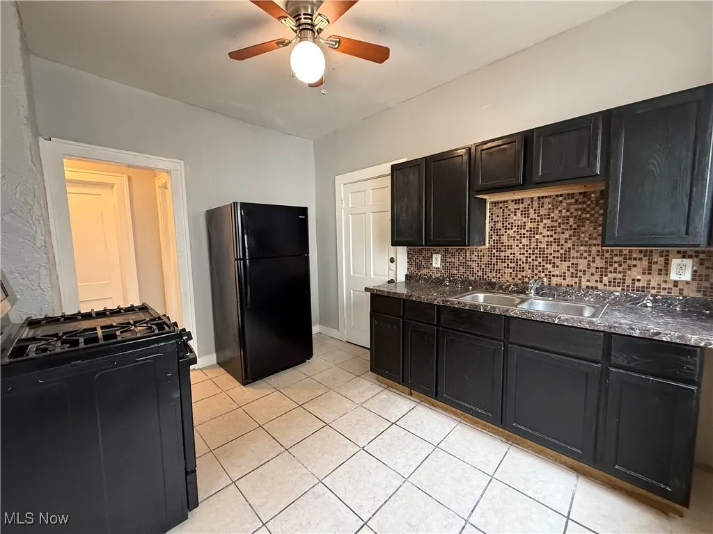 Kitchen with black appliances, dark cabinets, dark countertops, and tasteful backsplash
