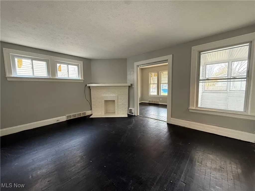 Unfurnished living room featuring a textured ceiling, dark wood-style flooring, and a brick fireplace